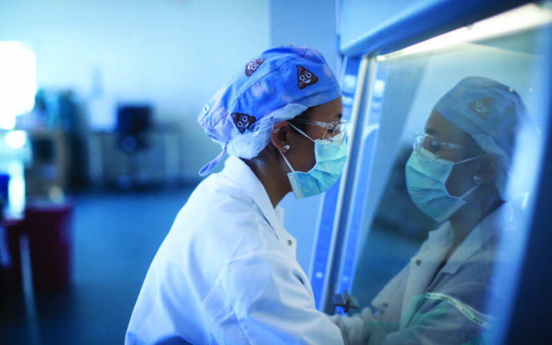 A scientist in lab attire analyzing a stool sample in a sterile area
