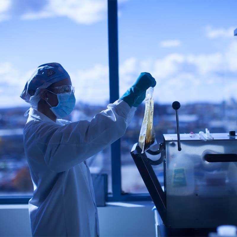 A scientist in lab attire holding a stool sample bag