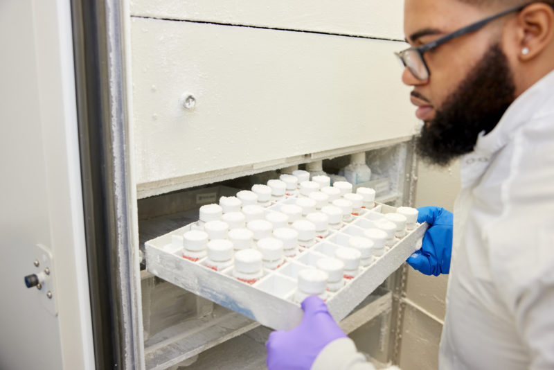 A laboratory technician removes a tray of bottles containing FMT capsules from a freezer.